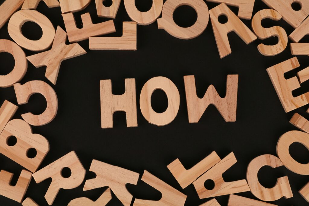 Wooden letters forming the word “HOW” on a black background, representing the question of how to evaluate the Best SEO Agency in Mumbai in a step-by-step guide.